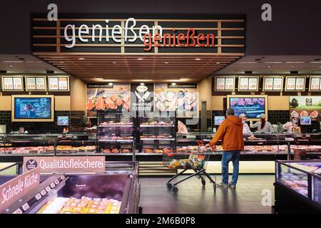 Homme dans une veste orange et un chariot à provisions devant le comptoir de service pour le fromage, la viande et les produits de saucisse, Famila Nordost Warenhaus Banque D'Images