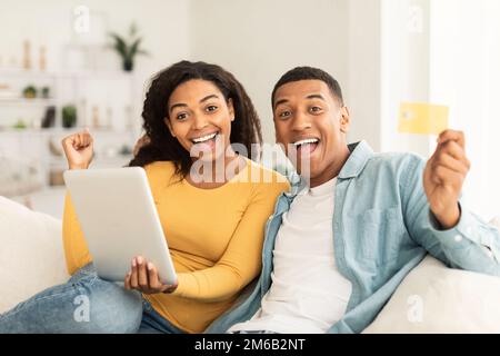 Heureux surpris couple afro-américain millénaire utiliser une tablette et une carte de crédit pour faire des achats en ligne Banque D'Images