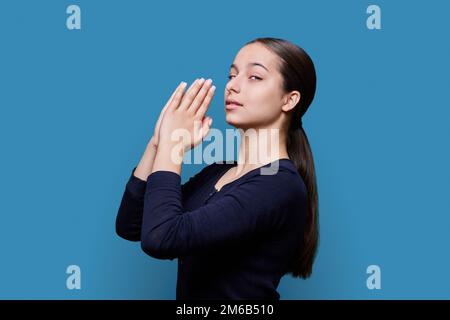 Jeune femme pleurait, tenant les mains dans la prière sur fond bleu, vue de profil Banque D'Images