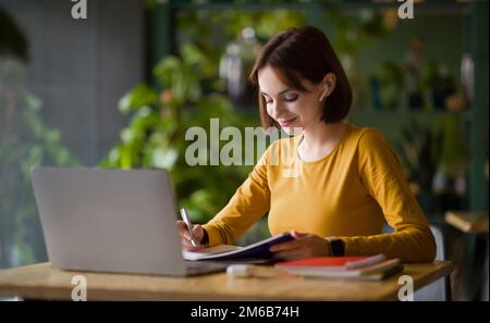 Jeune femme assise au café, prenant des notes dans le carnet Banque D'Images