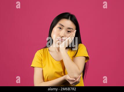 Laiteuse jeune chinoise se sentant contrariée et déprimée, regardant la caméra, posant sur fond rose Banque D'Images