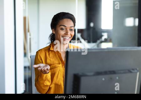 Une femme entrepreneur noire positive se gesticulant à l'ordinateur webcamera, travaillant et ayant l'appel vidéo au bureau Banque D'Images