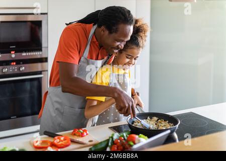 Papa noir affectueux et enfant femme préadolescent cuisant ensemble dans la cuisine Banque D'Images