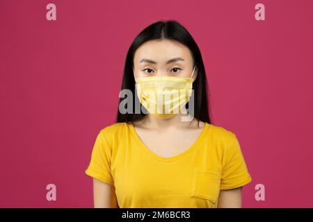 Concept des soins de santé et de la grippe. Portrait d'une jeune femme chinoise portant un masque chirurgical, fond de studio rose Banque D'Images