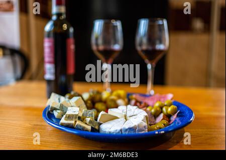 Hors-d'œuvre préparés avec une bouteille de vin rouge. Une assiette remplie de différents types de fromage, d'olives, de poivrons, de saucisses, d'ail et de concombre et d'un bot Banque D'Images
