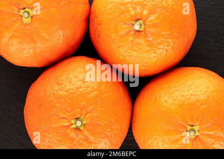 Quatre tangerines juteuses sur pierre d'ardoise, macro, vue de dessus. Banque D'Images