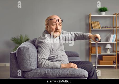 Homme senior tenant un bâton de marche tout en étant assis sur un canapé Banque D'Images