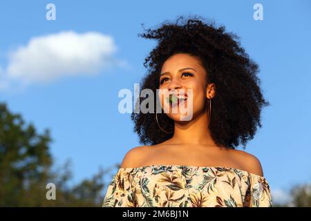 Belle fille africaine avec cheveux bouclés manger une fraise Banque D'Images