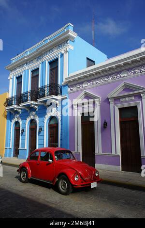 Une Volkswagen Beetle rouge vif passe devant des maisons du patrimoine violet et bleu restaurées sur la Calle 59, une rue célèbre de Merida Centro, Yucatan, Mexique Banque D'Images