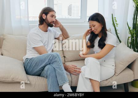 Un homme et une femme de différentes races s'assoient sur le canapé dans une pièce à la maison et parlent de leurs problèmes les uns aux autres. Un style de vie de famille sans stress Banque D'Images