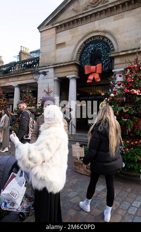 Jeune femme musulmane avec foulard regardant un téléphone portable portant une veste en fourrure blanche à Covent Garden marché heure de Noël Londres Royaume-Uni 2022 KATHY DEWITT Banque D'Images