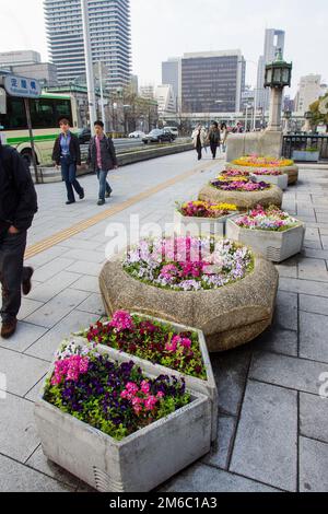 03-29-2015 Osaka, Japon. Lits de fleurs fins dans des vasons en béton à Osaka. Les gens qui marchent le dimanche. Paysage urbain avec gratte-ciel. À droite - ancienne lanterne Banque D'Images