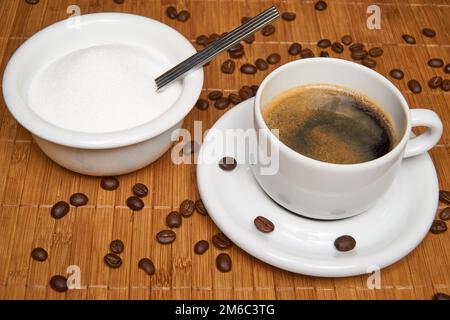 Tasse de café avec du sucre entouré par les grains de café sur un fond de bois. Banque D'Images