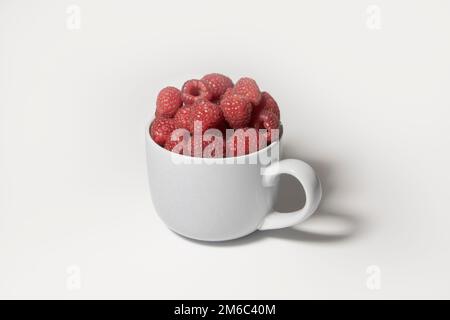 Baies de framboises dans un grand mug gris sur fond blanc Banque D'Images