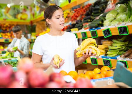 Une jeune femme positive qui choisit les bananes en magasin Banque D'Images