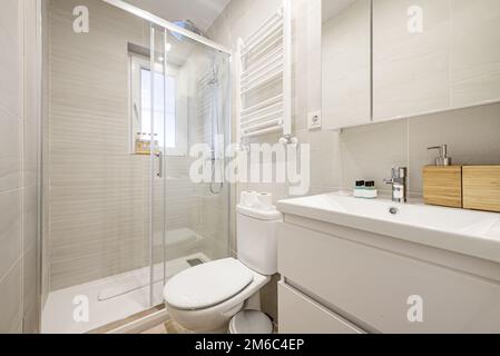 Petite salle de bains avec lavabo en porcelaine blanche sur une commode en bois avec armoires à portes vitrées et cabine de douche à parois de verre Banque D'Images