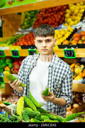 Un jeune acheteur de sexe masculin ciblé choisit le concombre indien momordica dans un magasin d'alimentation agricole Banque D'Images