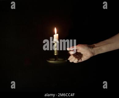 Chandelier décoratif en cuivre avec bougies allumées dans une main femelle sur fond noir Banque D'Images