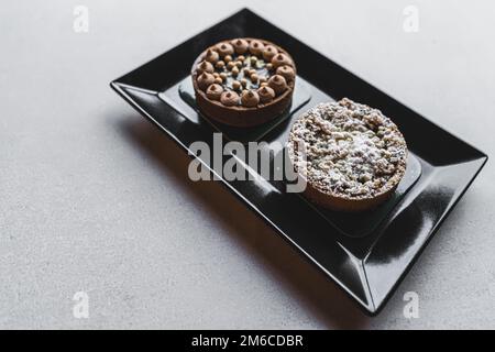 Deux mini-tartes décorées de crème et de sucre en poudre placées sur une assiette rectangulaire noire. Photo de haute qualité Banque D'Images