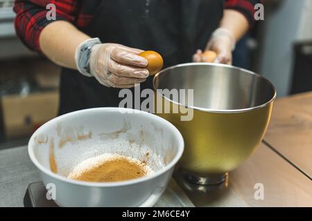Un chef de pâtisserie caucasien méconnaissable fendre un œuf sur la brime d'un bol mélangeur en acier inoxydable. Recette de cupcake. Photo de haute qualité Banque D'Images