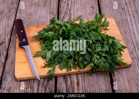 Planche à découper avec bouquet de persil frais et couteau de cuisine sur une table en bois. Mise au point sélective. Banque D'Images