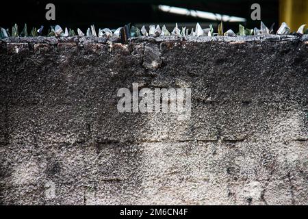 Mur de blocs de béton avec des couteaux en verre sur le dessus. Banque D'Images