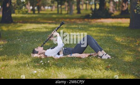 Une fille joue la clarinette en étant couché sur l'herbe dans le parc. Banque D'Images