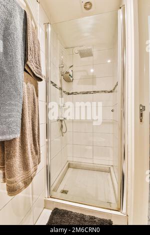 une salle de bains avec des serviettes accrochées au mur et une porte de douche en verre dans le coin, à côté d'un porte-serviettes Banque D'Images