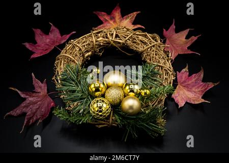 Torchez de Noël avec des boules dorées et des feuilles rouges séchées sur du noir. Banque D'Images