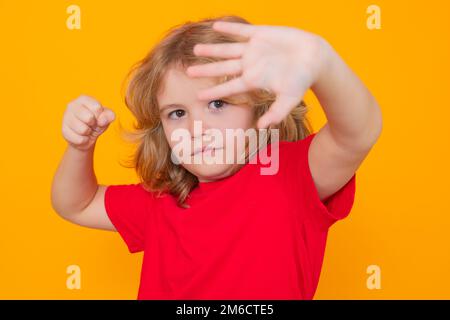 Enfant garçon dans un t-shirt rouge faisant un geste d'arrêt sur un arrière-plan de studio isolé. Enfant avec le combat gestuel poing. Protection des enfants, intimidation, abus et violence Banque D'Images