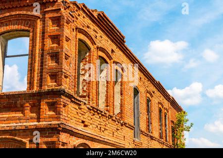 Une grande maison ancienne ruinée de briques rouges contre un ciel bleu avec des nuages blancs. Banque D'Images