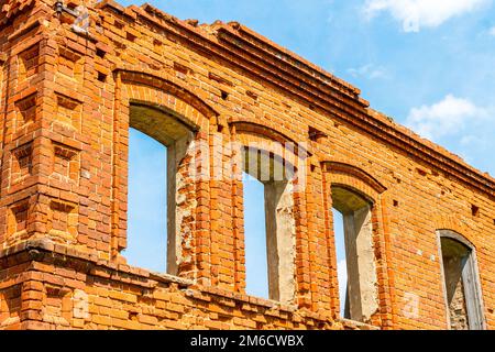 Une grande maison ancienne ruinée de briques rouges contre un ciel bleu avec des nuages blancs. Banque D'Images