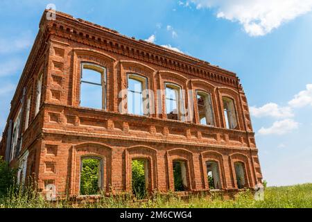 Une grande maison ancienne ruinée de briques rouges contre un ciel bleu avec des nuages blancs. Banque D'Images