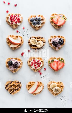 Mini-gaufres en forme de cœur avec diverses garnitures de pâtes à tartiner et fruits frais. Banque D'Images