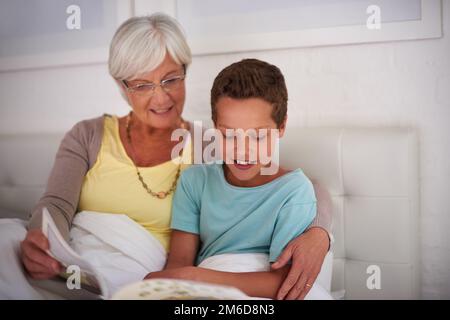 Story Time avec gran. Une grand-mère lisant un livre à son petit-fils au lit. Banque D'Images