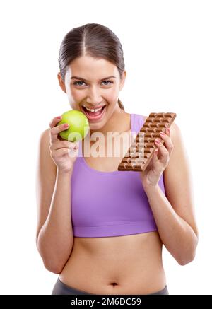 Vous gagnez votre corps. une jeune femme en forme tenant une pomme d'une main et du chocolat de l'autre. Banque D'Images