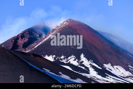 Gros plan sur le cratère du sommet de l'Etna qui émet des fumées, avec des pentes couvertes de soufre et de neige, un volcan actif populaire en Sicile, en Italie Banque D'Images