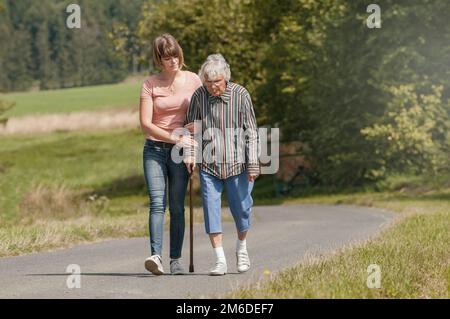 Jeune femme aide senior woman walking with stick Banque D'Images