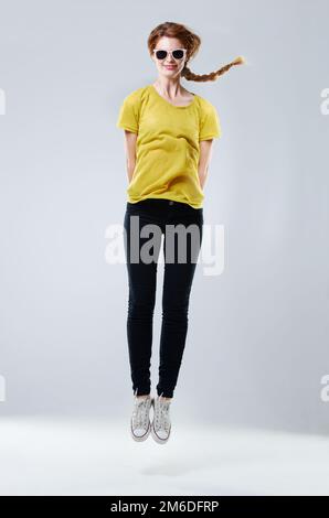 Shes un esprit libre. Studio portrait d'une belle jeune femme en vêtements décontractés sautant sur fond gris. Banque D'Images