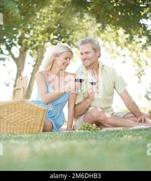 Heres à notre amour. Un mari et une femme heureux de goûter avec un verre de vin pendant qu'ils aiment pique-niquer à l'extérieur dans un parc le jour de l'été. Banque D'Images