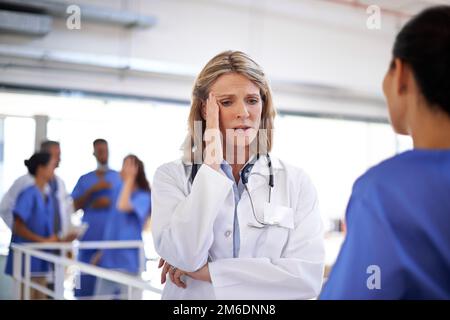 Cela a été un long changement à l'hôpital. un médecin surtravaillé parlant à une infirmière dans un couloir d'hôpital. Banque D'Images