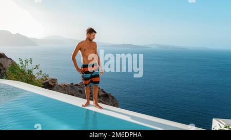 Santorini Grèce Oia, jeunes hommes en short de bain se détendre dans la piscine donnant sur la caldeira de l'île de Santorini Grèce, piscine à débordement, un jeune homme sur des vacances de luxe en Europe Grèce Banque D'Images