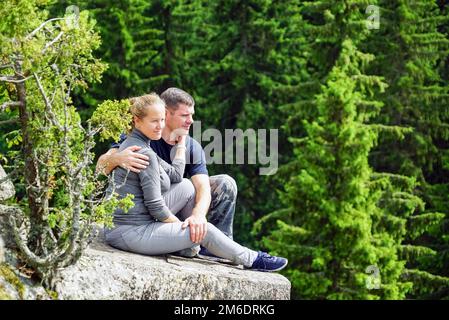 Un homme et une femme s'assoient en s'embrassant sur le bord d'une montagne dans la nature . Banque D'Images