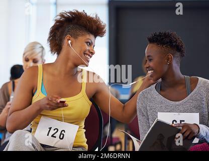 Partager des morceaux pendant qu'ils attendent. deux danseuses féminines écoutant de la musique tout en attendant une audition de danse. Banque D'Images