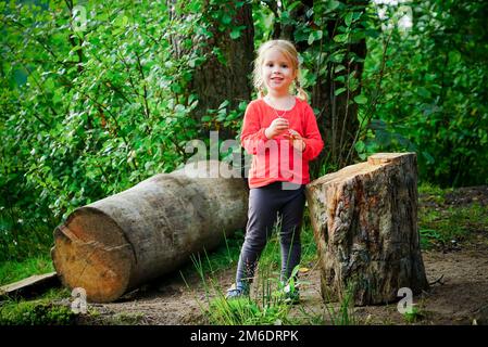 Une petite fille gaie de 3 ans se tient près d'une bûche dans la forêt. Banque D'Images