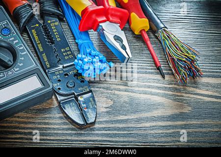 Testeur électrique, tournevis, fils, serre-câbles, pinces coupantes à boulon, voltmètre sur panneau en bois. Banque D'Images