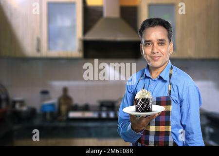 Chef masculin indien avec un gâteau sucré avec des intérieurs de cuisine Banque D'Images