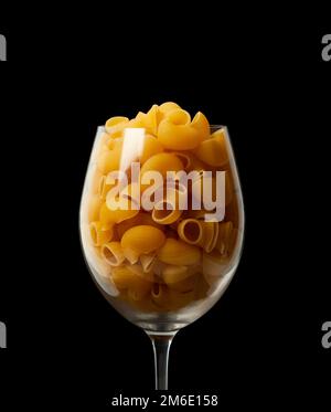 Tuyau de pâtes Rigate dans une tasse en verre isolée sur fond noir Banque D'Images
