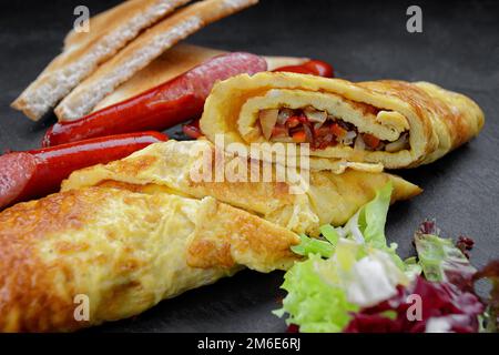 Petit déjeuner, omelette frite avec légumes, saucisses frites et pain grillé sur une pierre noire Banque D'Images