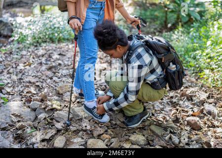 Sac à dos voyage touristique randonnée aventure aider un ami attacher la chaussure près de l'eau du ruisseau Banque D'Images